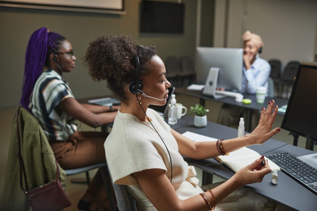 Three multicultural professionals collaborating at a modern call center, wearing headsets and working at computers.